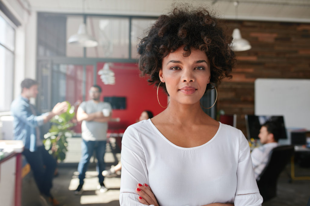 Portrait of woman standing in busy creative office looking at camera. Attractive female creative professional in design studio.