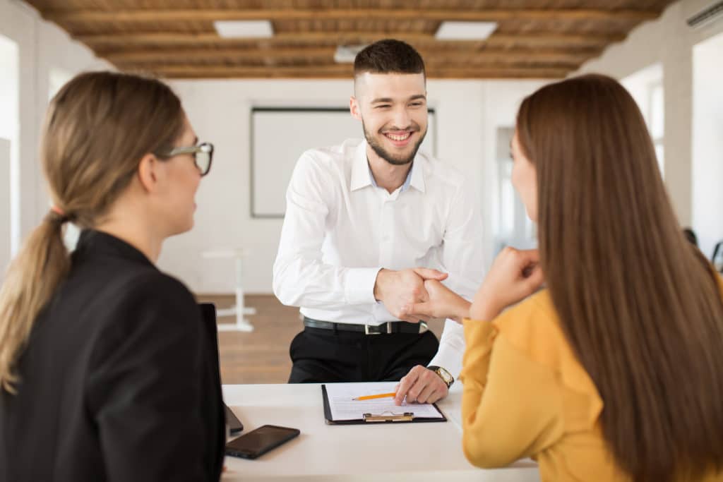 Cheerful male applicant happily shaking employer hand.