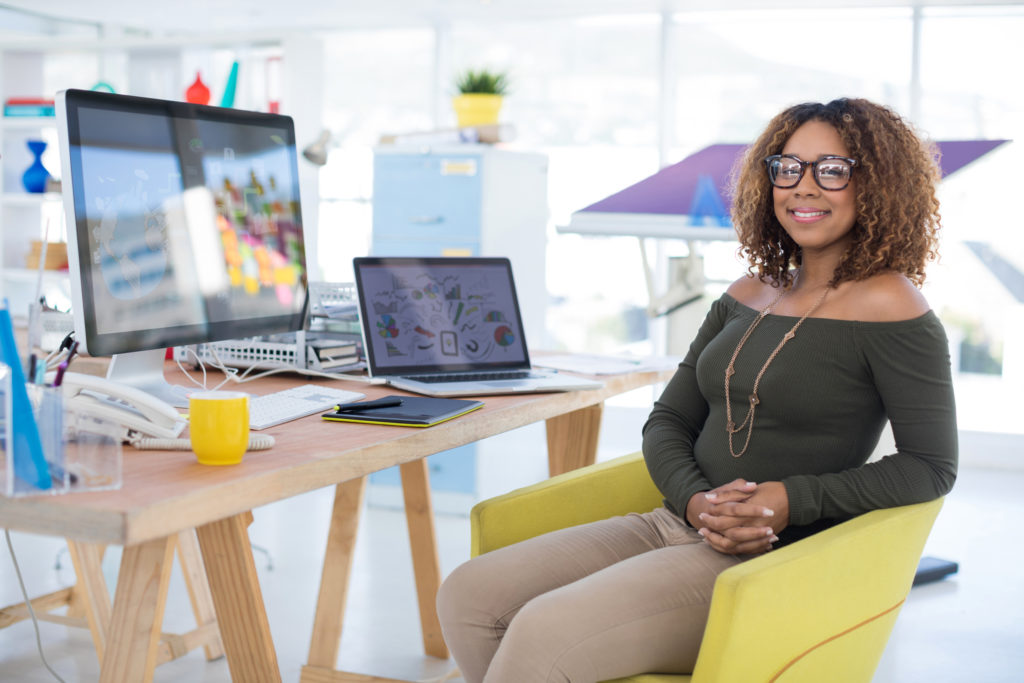 Happy lady wearing a green shirt while sitting in a yellow chair at her desk.